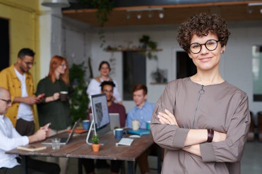 pexels-photo-3184405-3184405 Smiling businesswoman with curly hair stands confidently in a modern office space with colleagues.